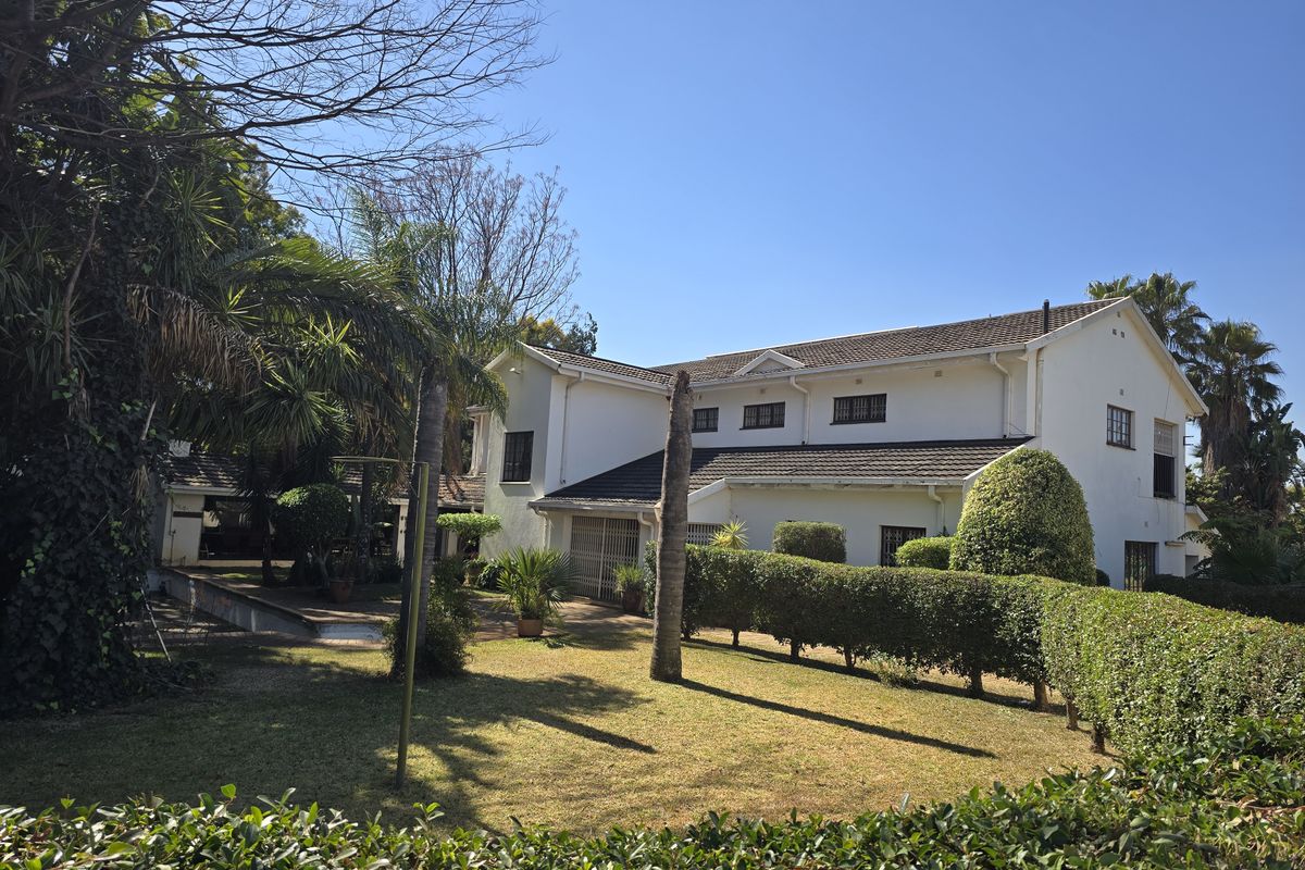 A view of the rear elevation of the house featuring a well-maintained garden, manicured hedges, and a tiled roof structure.