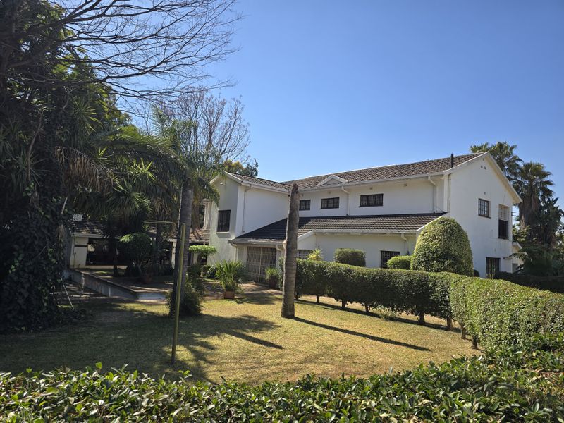 A view of the rear elevation of the house featuring a well-maintained garden, manicured hedges, and a tiled roof structure.
