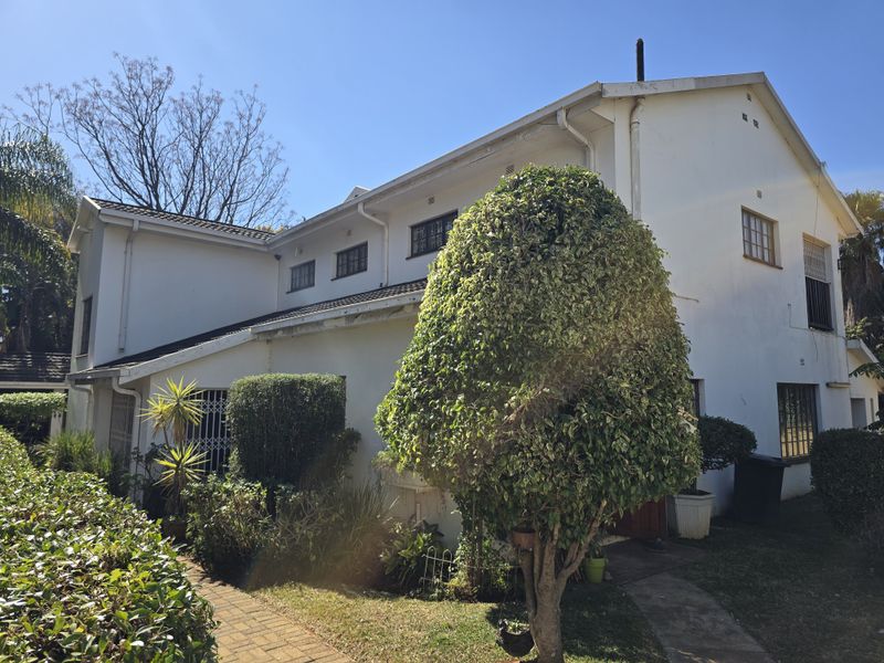 Rear exterior view of a two-story house featuring white painted walls, security bars on windows, and a paved garden walkway.