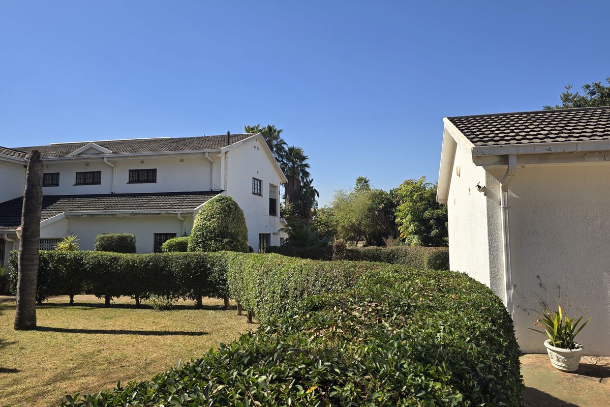 A view of the rear garden area featuring well-maintained hedges, lawn, and the exterior facade of the main house and an outbuilding.