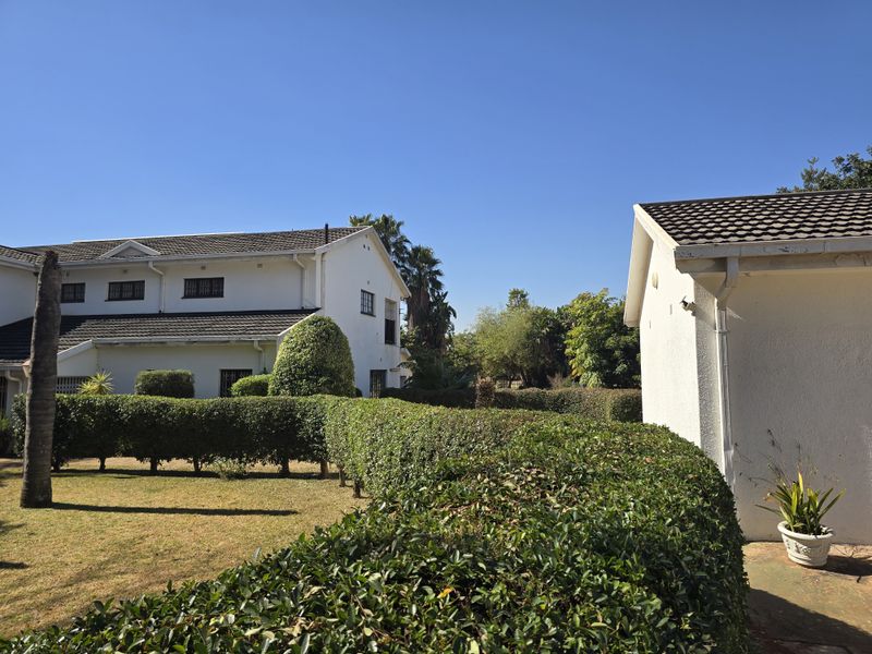 A view of the rear garden area featuring well-maintained hedges, lawn, and the exterior facade of the main house and an outbuilding.