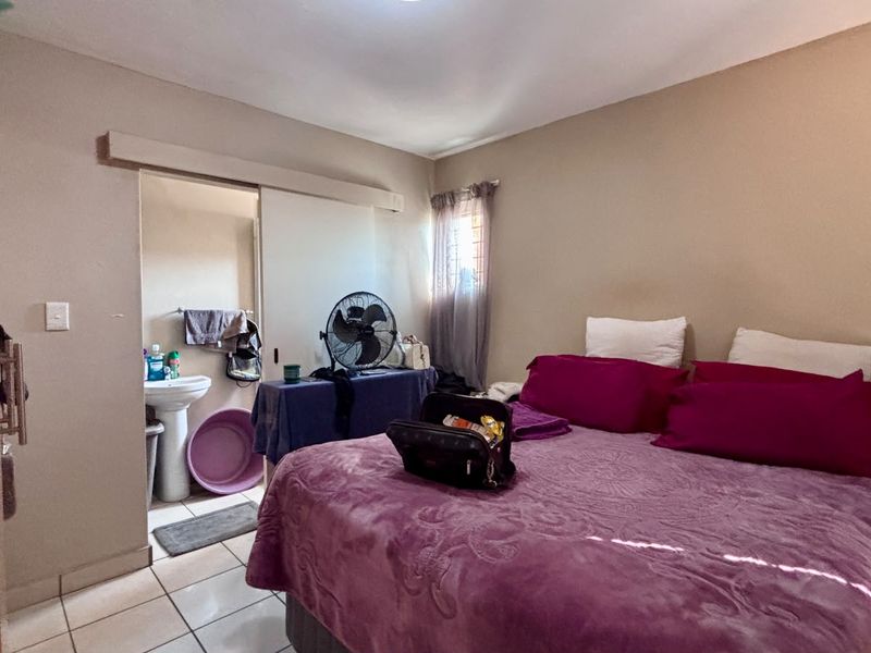 A bedroom featuring tiled flooring, a built-in cupboard, and an en-suite area with a pedestal basin.