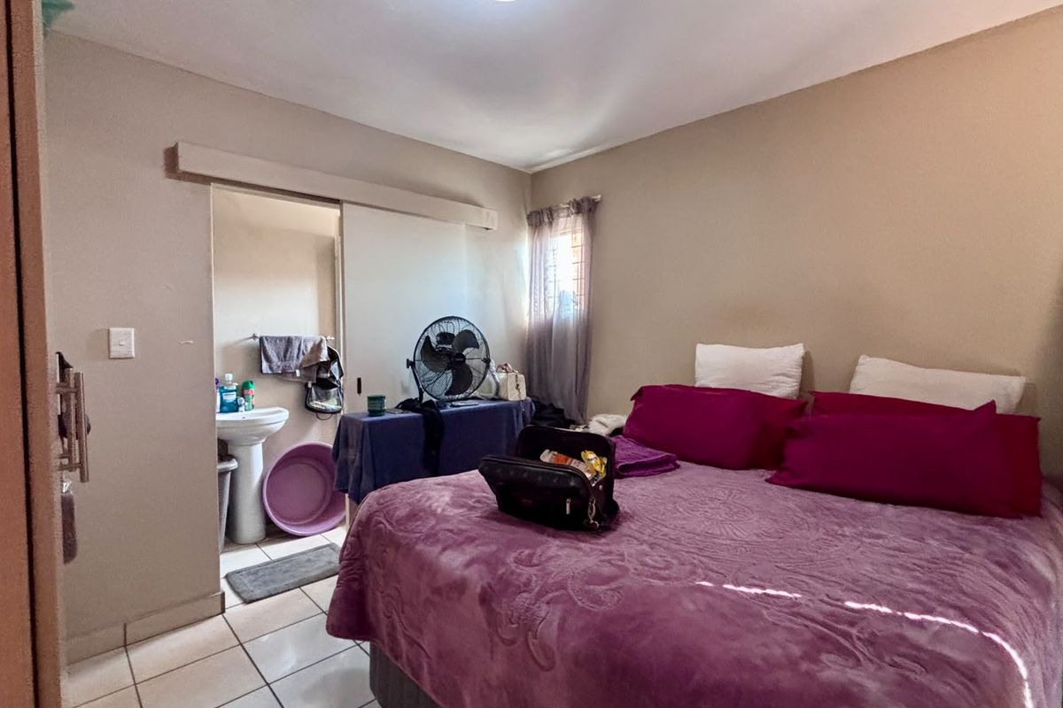 A bedroom featuring tiled flooring, a built-in cupboard, and an en-suite area with a pedestal basin.