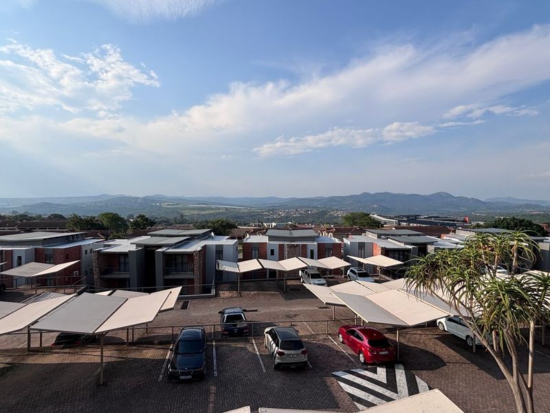 Elevated view overlooking a residential apartment complex with paved parking areas and shade cloth carports against a scenic mountain backdrop.