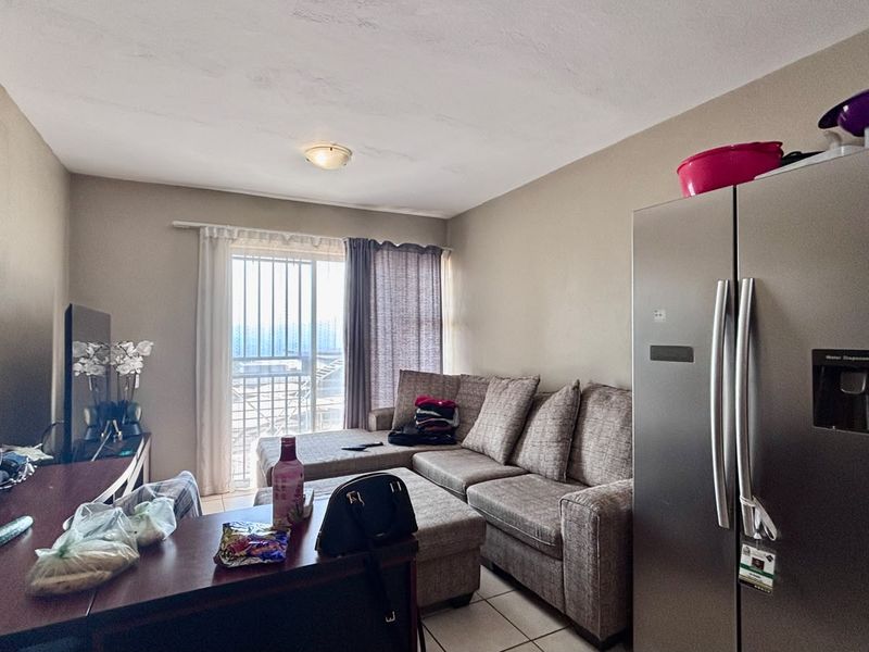 Open plan living area featuring tiled flooring and a sliding glass door with security gate, providing access to the balcony.