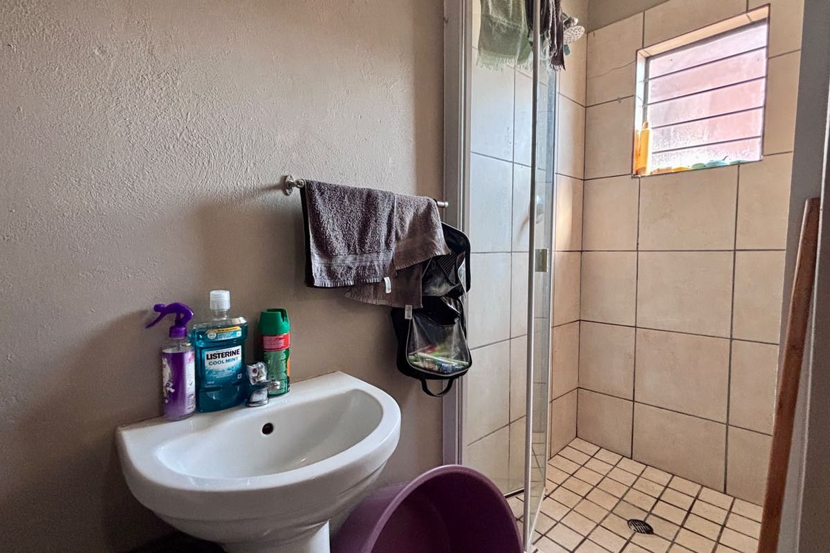 Compact bathroom featuring a pedestal basin and a separate shower enclosure with tiled finishes and a small window.
