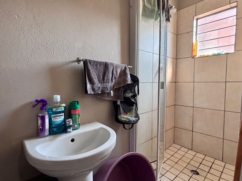 Compact bathroom featuring a pedestal basin and a separate shower enclosure with tiled finishes and a small window.