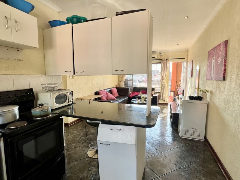 Open-plan kitchen and living area featuring tiled floors, a breakfast bar, and built-in cabinetry, leading to an outdoor balcony space.