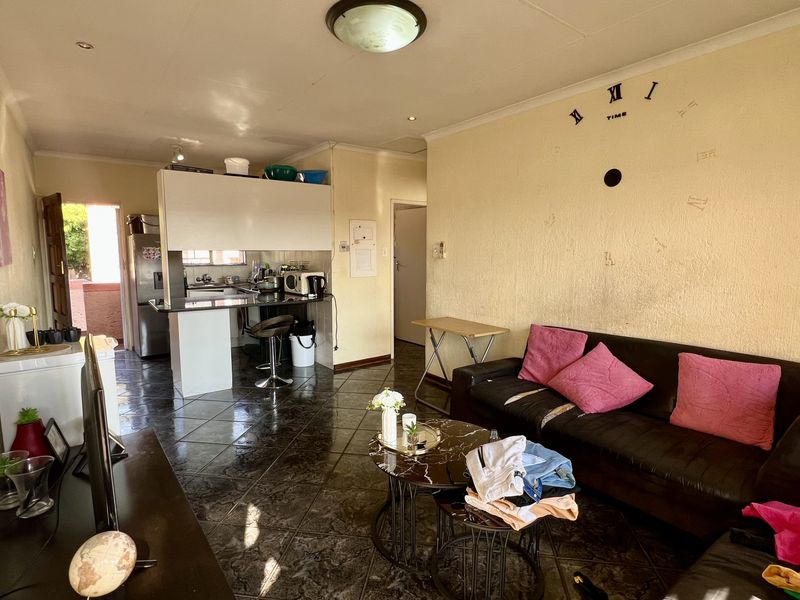 Open-plan living and kitchen area featuring tiled flooring and a compact kitchen layout, requiring cosmetic updates to improve the overall aesthetic.