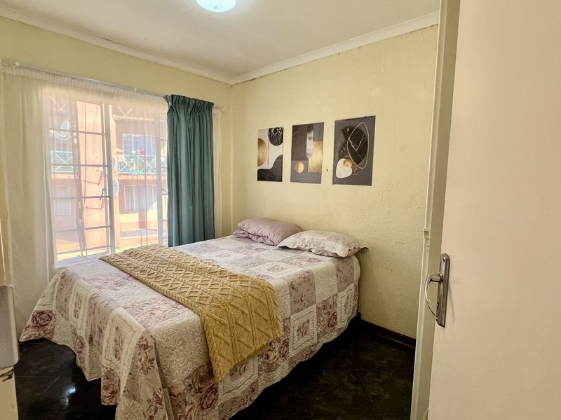 A compact bedroom featuring tiled flooring, a window with security bars, and neutral wall finishes, offering a functional space for rest.