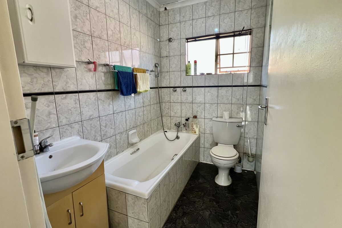 A functional bathroom featuring a bathtub, toilet, and vanity basin with tiled walls and flooring, offering a dated but well-maintained layout.