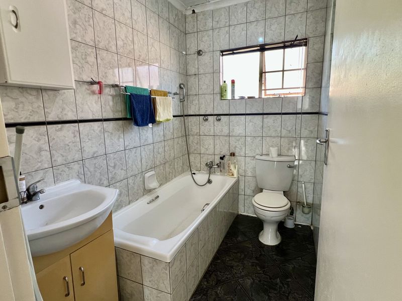 A functional bathroom featuring a bathtub, toilet, and vanity basin with tiled walls and flooring, offering a dated but well-maintained layout.