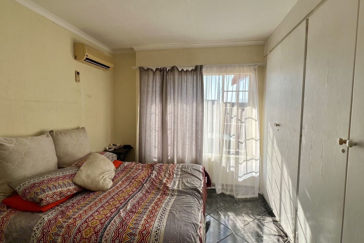 A functional bedroom featuring built-in cupboards, tiled flooring, and an installed air conditioning unit, offering a practical layout with natural light.