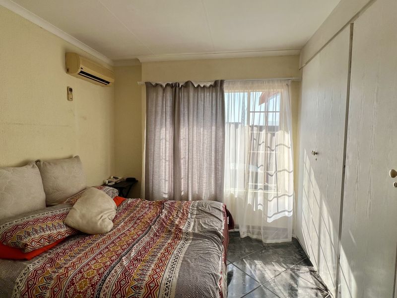 A functional bedroom featuring built-in cupboards, tiled flooring, and an installed air conditioning unit, offering a practical layout with natural light.