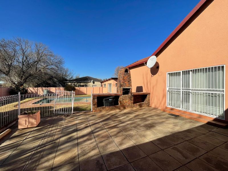 Outdoor patio area featuring a built-in brick braai, paved flooring, and direct access to the swimming pool and garden.