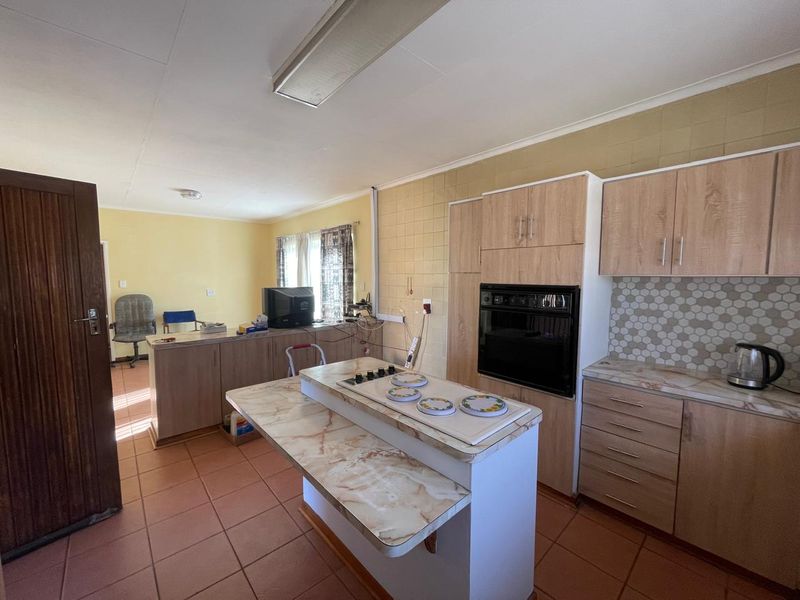 Open-plan kitchen featuring wood-look cabinetry, built-in oven, hob, and tiled flooring, offering a functional layout with potential for modern updates.