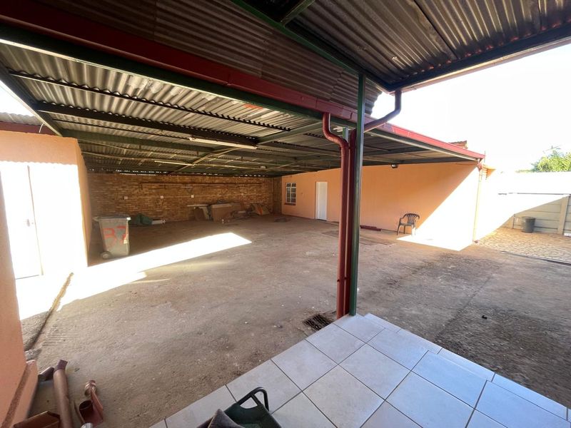 A large, covered outdoor patio area featuring a corrugated metal roof, exposed brick wall, and concrete flooring, suitable for an outdoor entertainment space.