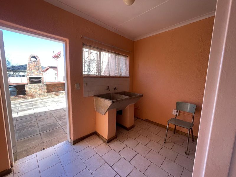 A functional laundry area featuring a traditional concrete double sink, tiled flooring, and direct access to an outdoor patio with a built-in brick braai.