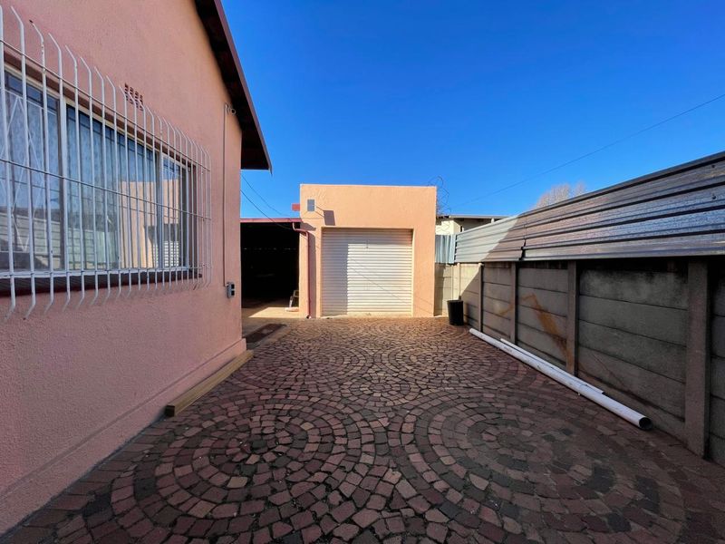 Rear exterior area featuring cobblestone paving, a single garage door, and secure boundary walling with corrugated metal fencing.