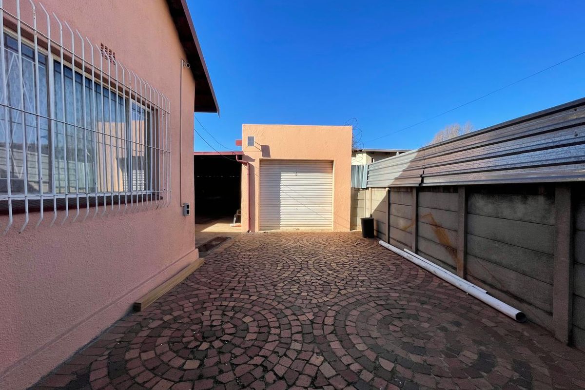 Rear exterior area featuring cobblestone paving, a single garage door, and secure boundary walling with corrugated metal fencing.
