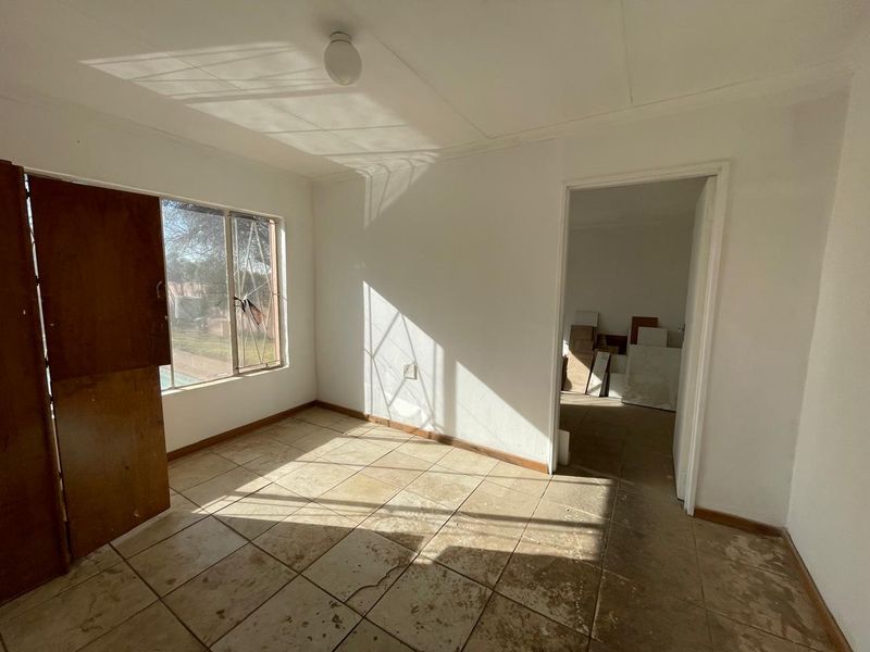 An empty bedroom featuring tiled flooring and a window, requiring cosmetic updates and repairs to the flooring and window frame.