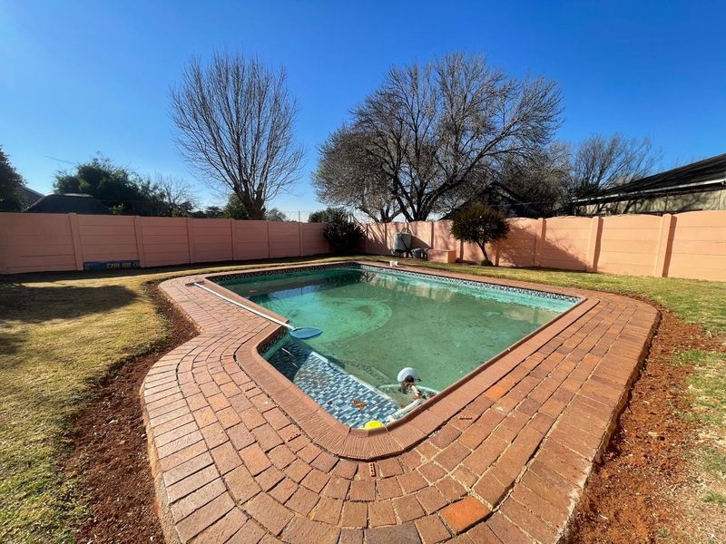 Outdoor swimming pool area featuring brick paving surround and perimeter boundary wall in a spacious backyard setting.