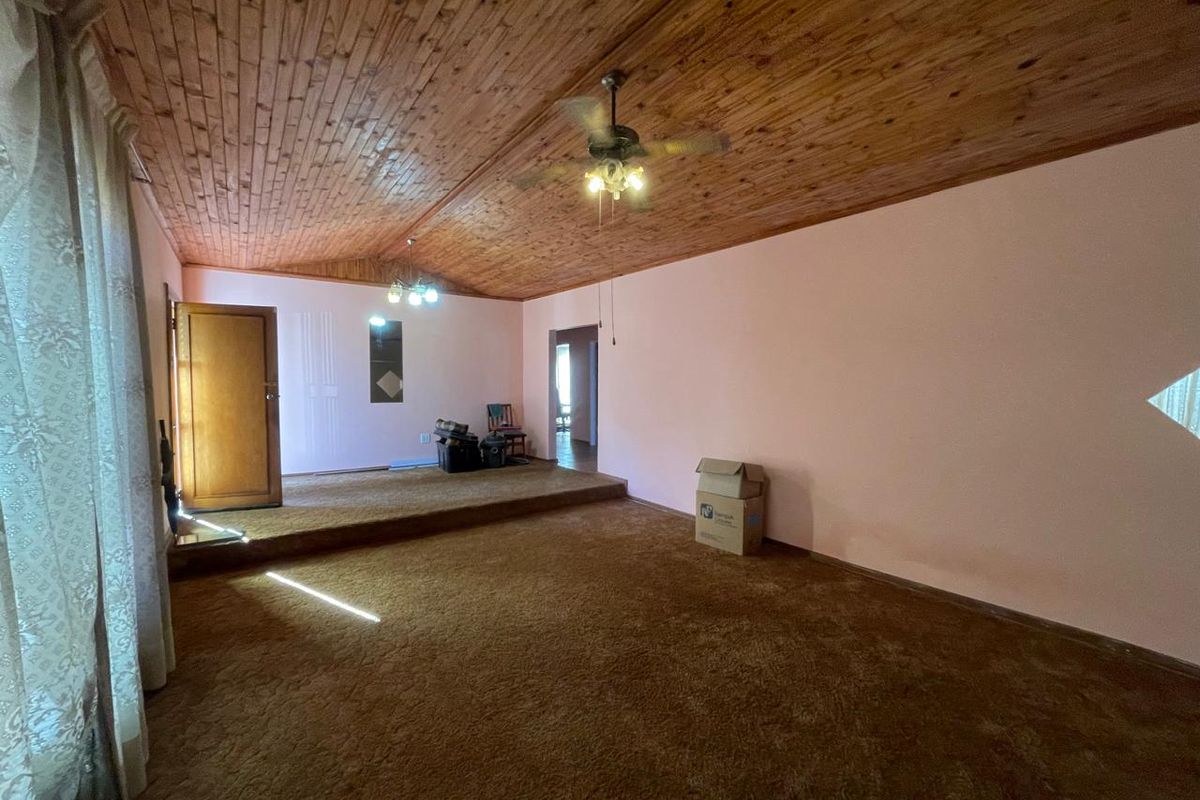 Spacious living area featuring a timber tongue and groove ceiling, ceiling fan, and a raised floor platform with carpeted flooring.