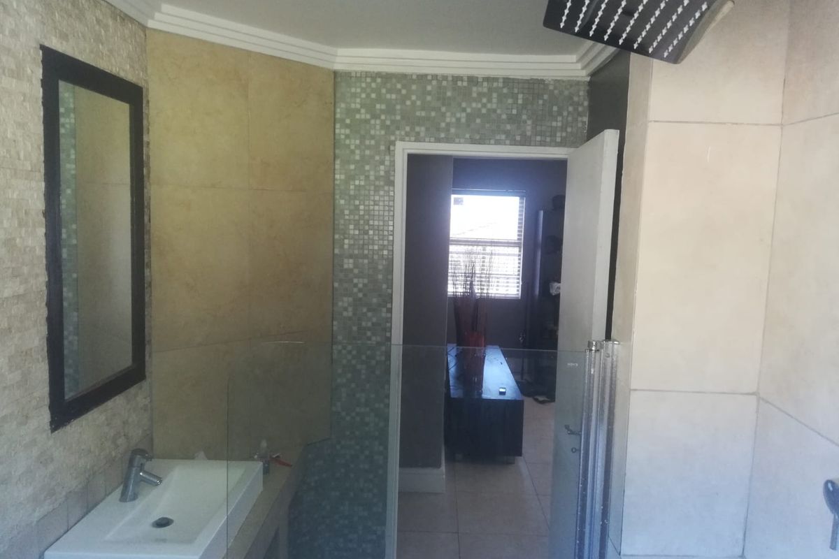 A bathroom featuring a wall-mounted basin, glass shower screen, and modern rain shower head with mosaic and large format wall tiling.