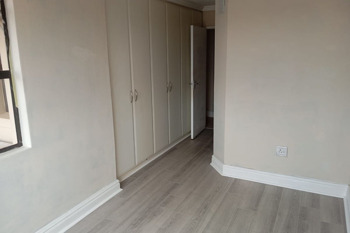 A vacant bedroom featuring light-toned laminate flooring, built-in cupboards, and neutral wall finishes, offering a clean canvas for personalization.