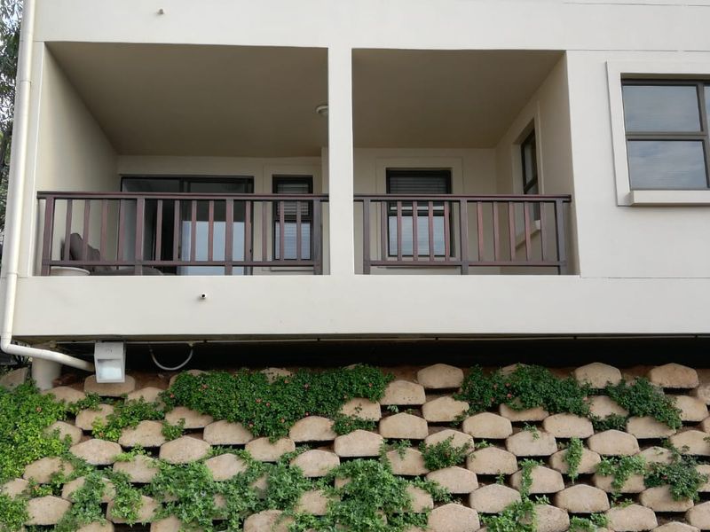 A view of the apartment balcony featuring a wooden railing, sliding glass doors, and a landscaped retaining wall below.