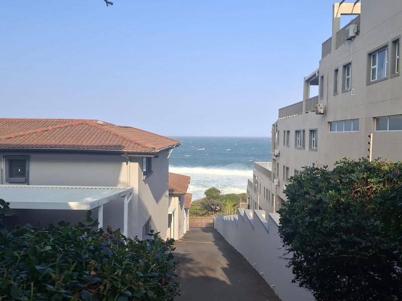 A view looking down a driveway between apartment buildings towards the ocean.