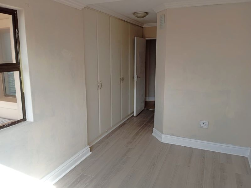 An empty bedroom featuring light-toned laminate flooring, built-in cupboards, and neutral wall finishes, providing a blank canvas for personalization.