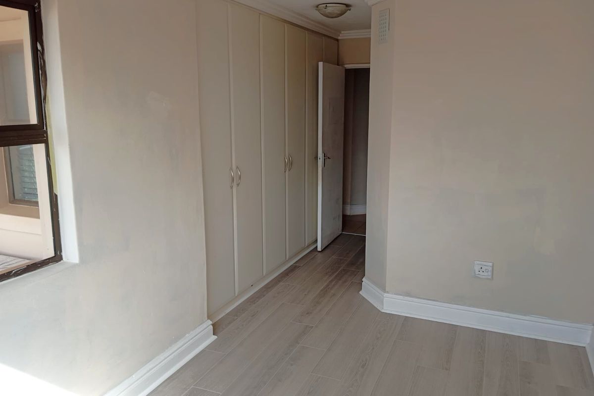 An empty bedroom featuring light-toned laminate flooring, built-in cupboards, and neutral wall finishes, providing a blank canvas for personalization.