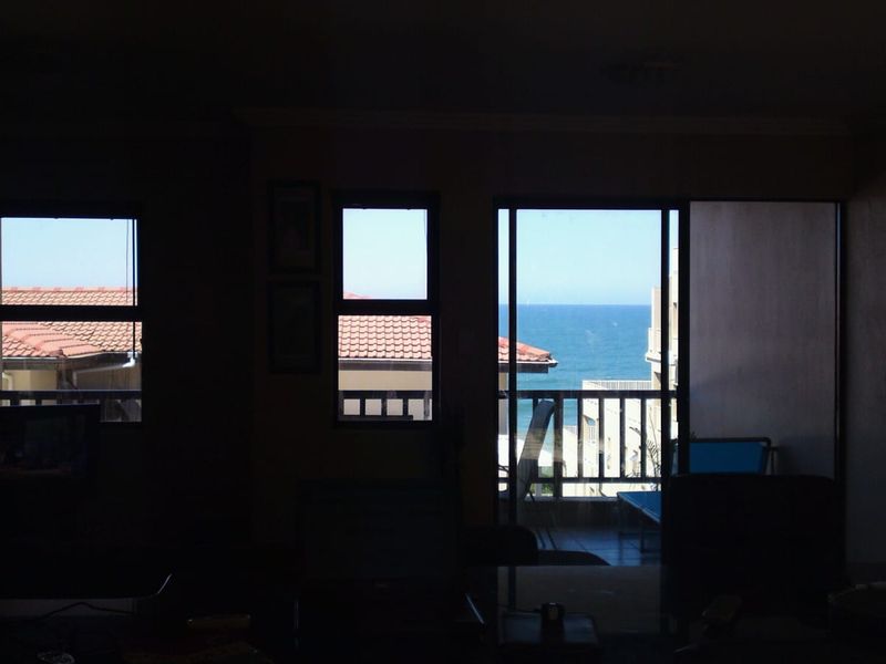 A dimly lit living area featuring sliding glass doors that open onto a balcony with ocean views.
