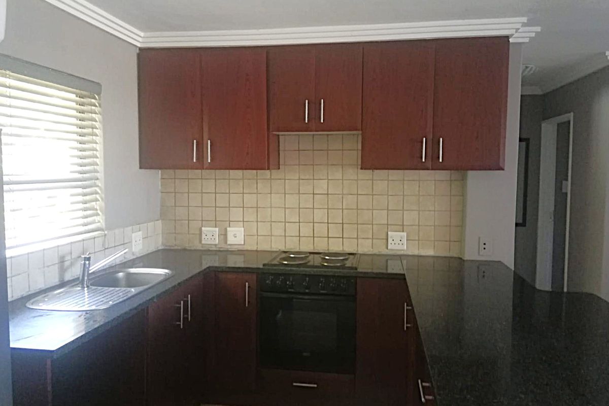 A functional kitchen featuring dark wood cabinetry, granite countertops, a built-in oven with hob, and a tiled backsplash.