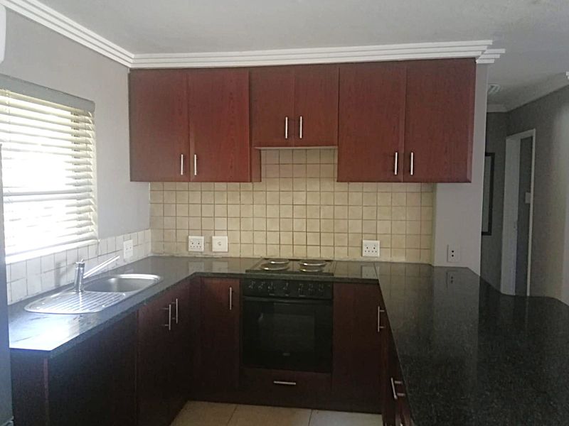 A functional kitchen featuring dark wood cabinetry, granite countertops, a built-in oven with hob, and a tiled backsplash.