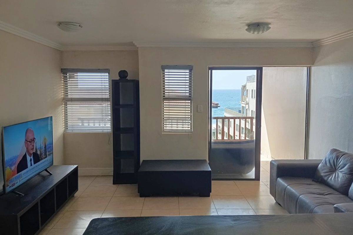 A living room featuring tiled flooring, sliding glass doors leading to a balcony, and views of the ocean.