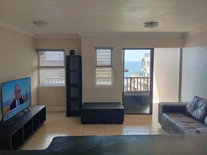 A living room featuring tiled flooring, sliding glass doors leading to a balcony, and views of the ocean.