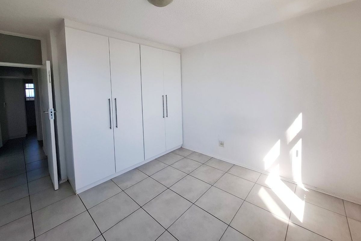 A bright, empty bedroom featuring neutral tiled flooring and clean white built-in cupboards, offering a versatile space ready for personalization.