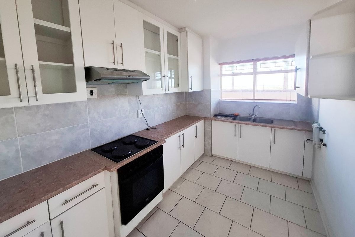 A functional kitchen featuring white cabinetry, a built-in electric stove with extractor fan, double sink, and tiled flooring.