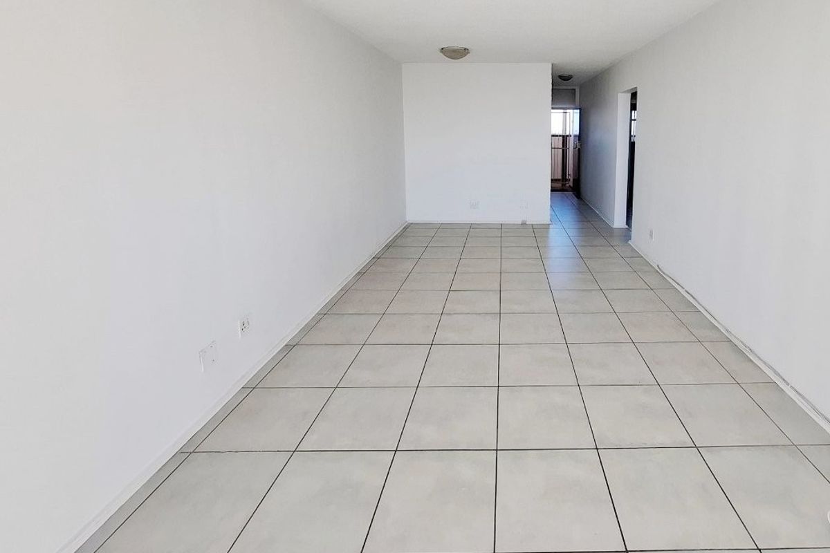 A spacious, empty living area featuring neutral ceramic floor tiles and clean white walls, offering a versatile blank canvas for interior design.