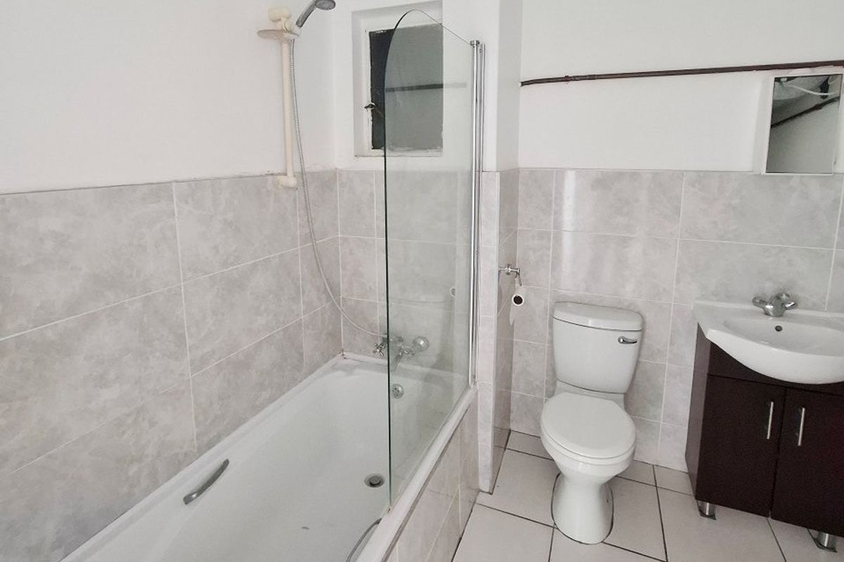 A functional bathroom featuring a bathtub with a glass screen, a toilet, and a vanity unit with a washbasin, finished with neutral wall and floor tiles.