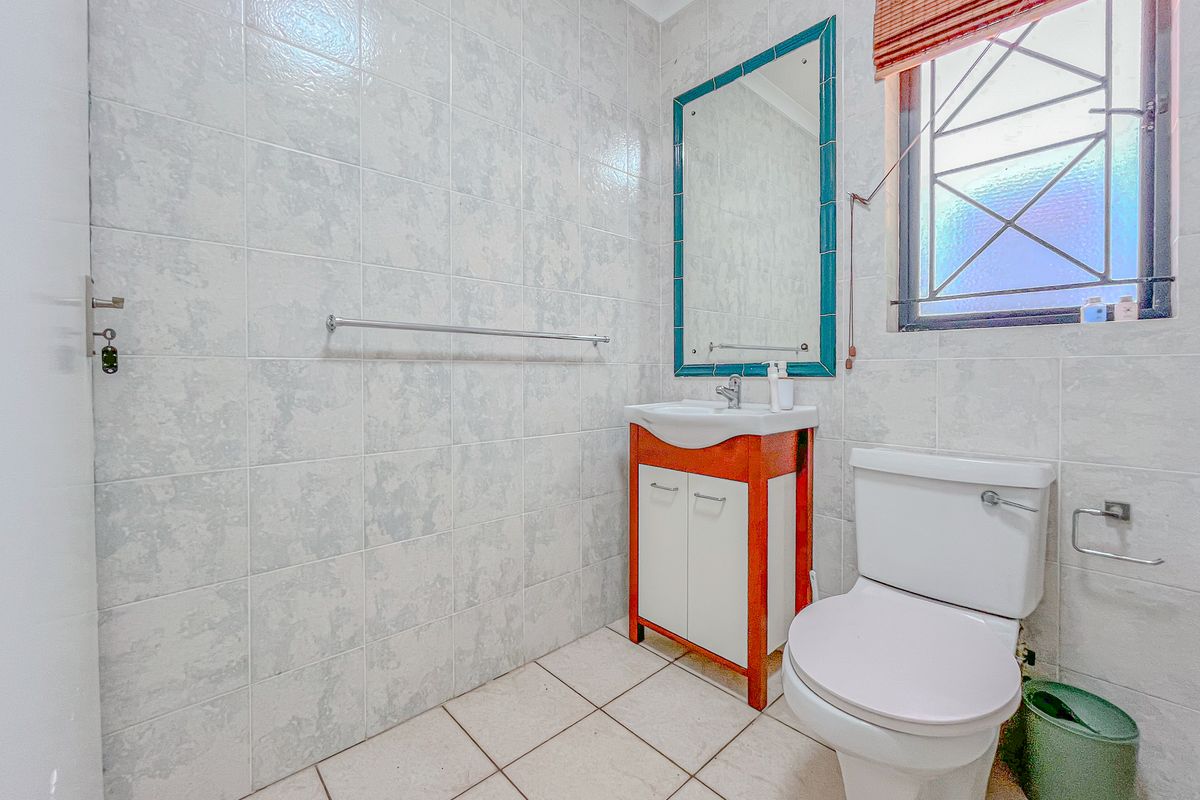 A functional bathroom featuring a vanity cabinet with basin, wall-mounted mirror, toilet, and full-height wall tiling with security bars on the window.