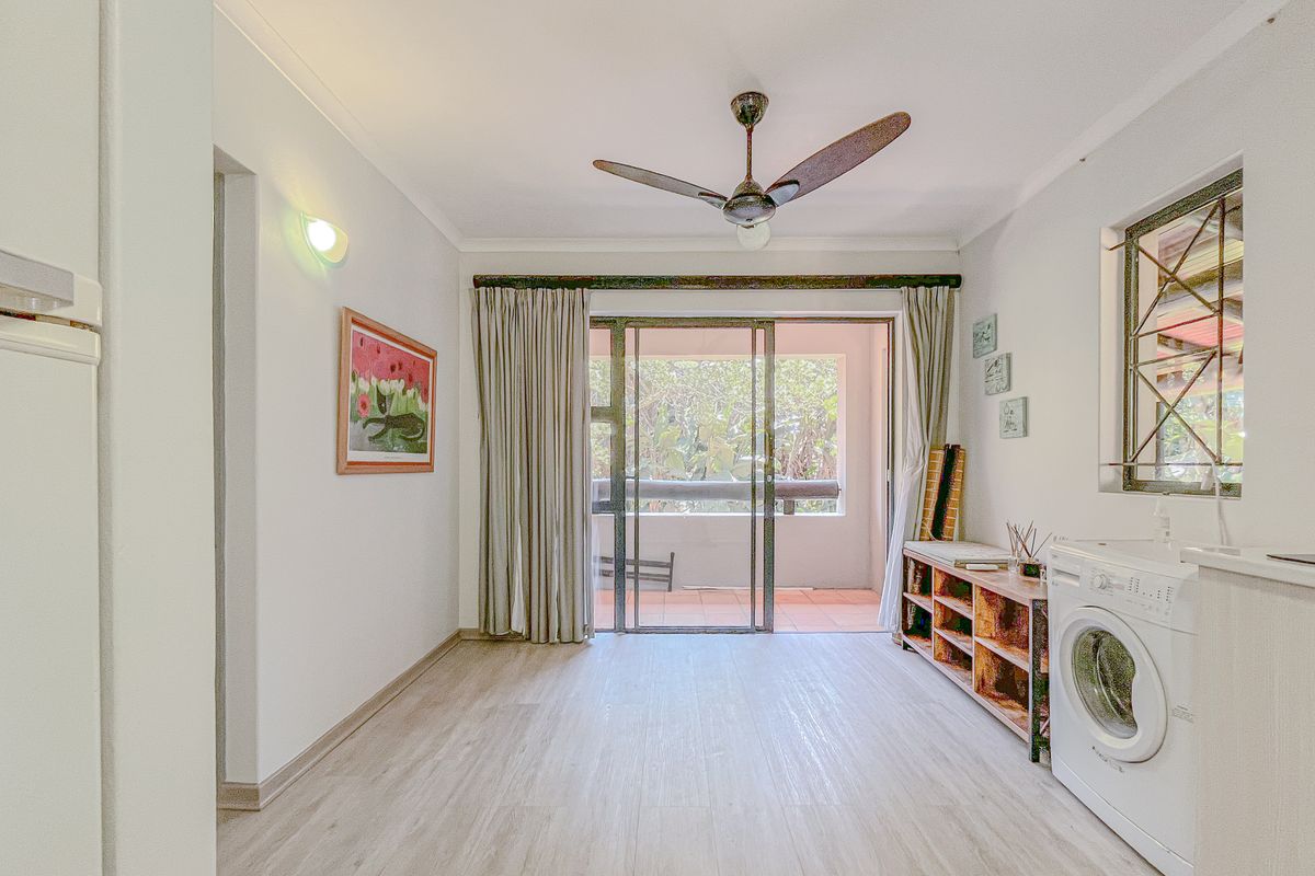 A bright living area featuring laminate flooring, a ceiling fan, and sliding glass doors that open onto a private balcony.