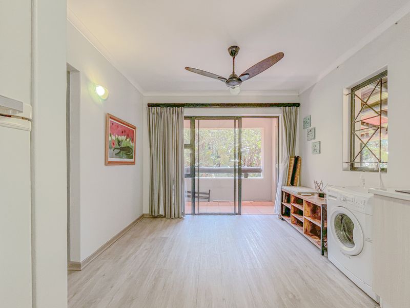 A bright living area featuring laminate flooring, a ceiling fan, and sliding glass doors that open onto a private balcony.