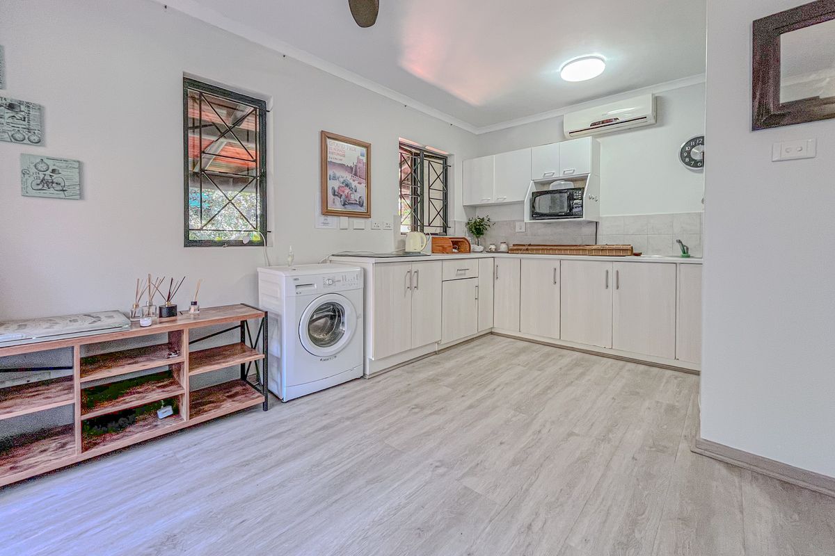 A functional kitchen featuring light-toned cabinetry, laminate flooring, integrated microwave, and a split-system air conditioner, with security bars on the windows.