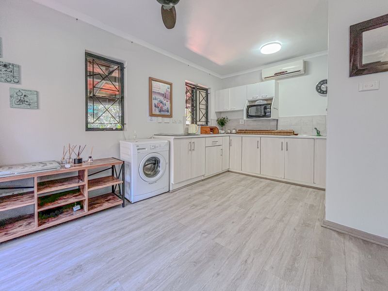 A functional kitchen featuring light-toned cabinetry, laminate flooring, integrated microwave, and a split-system air conditioner, with security bars on the windows.
