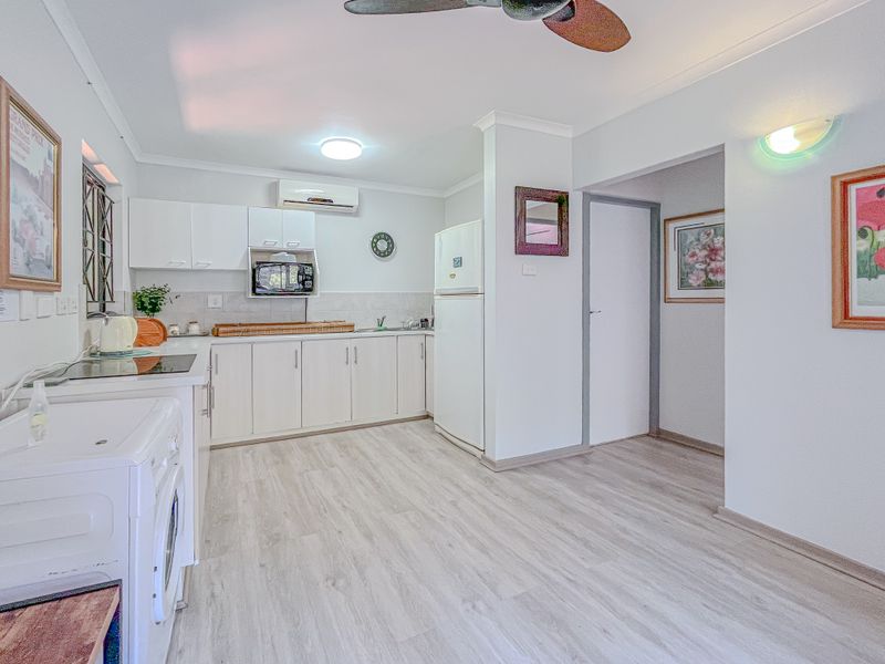 A functional kitchen featuring white cabinetry, laminate flooring, a built-in microwave, and a wall-mounted air conditioning unit.