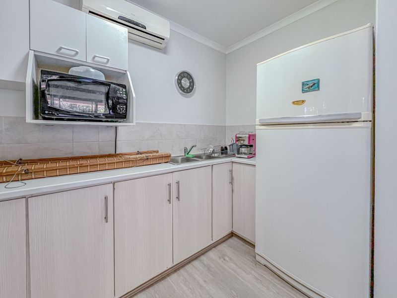 A functional kitchen featuring laminate cabinetry, a stainless steel double sink, tiled splashback, and a wall-mounted air conditioning unit.