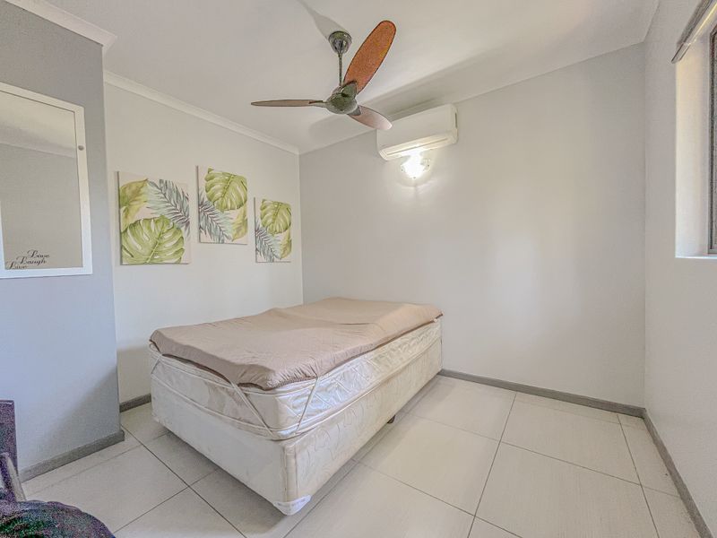 A bright bedroom featuring tiled flooring, a ceiling fan, and a wall-mounted split-system air conditioning unit.